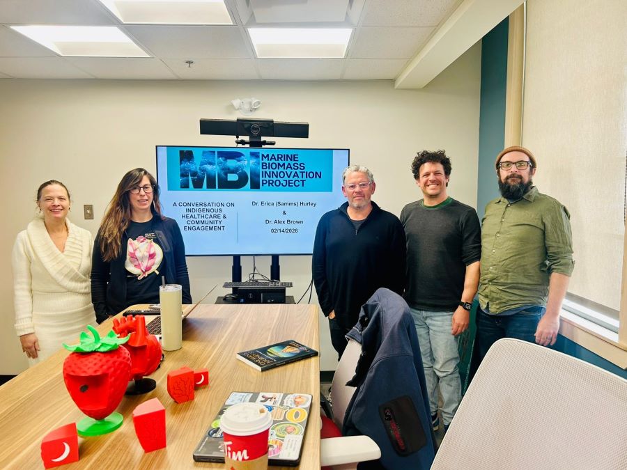 Five people in a meeting room standing in front of a presentation on a screen.