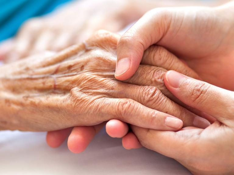 Elderly person's hand being held caringly by another pair of hands