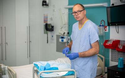 Person in hospital uniform and gloves standing next to a hospital bed