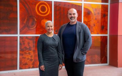 two people standing together with red glass wall behind