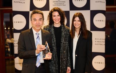 Person holding glass award with two people standing next to him, facing camera