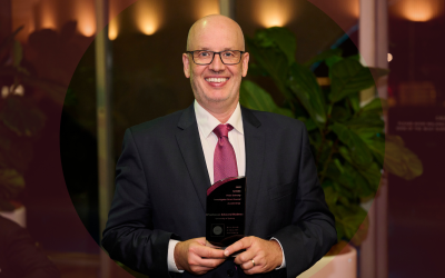 Man in suit with an award, smiling.