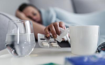 Sick person in bed reaching for a tissue and pain killers