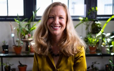 Professor Karen Canfell sitting down in front of a window and various pot plants